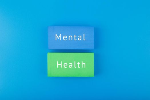 Creative flat lay with blue and green blocks with written mental health text on dark blue background. Concept of world mental health day, mental health assessment and awareness