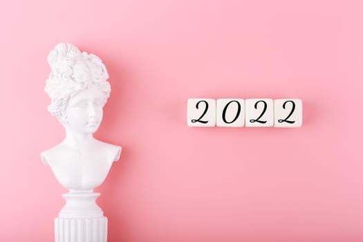 Creative trendy 2022 concept. Numbers written on white cubes next to white antique gypsum woman figure on bright pink background. New year resolution or plans concept