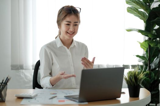 Smiling young female employee at home speak talk on video call on laptop with diverse colleagues. Asian woman worker have webcam conference or digital web team meeting or briefing with coworkers.