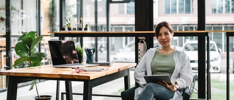 Portrait Of Attractive Asian Businesswoman Working On Laptop and digital tablet for marketing plan at her office.