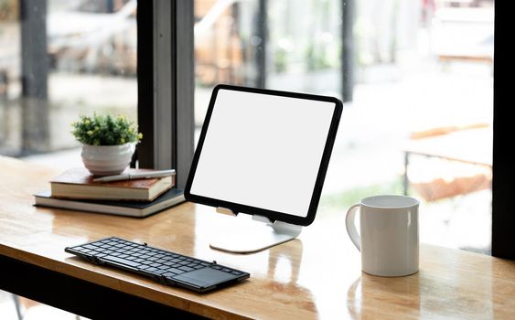 Portable workspace with blank screen tablet on wooden desk with copy space and decorations in coffee shop