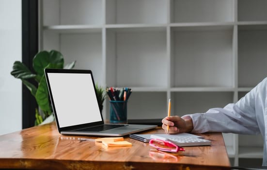 Close up business woman using laptop computer and making note on notepad in modern office