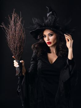 Charming halloween witch with broom over black background, woman beauty portrait, artistic make-up and costume
