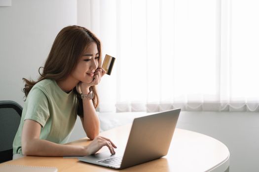 Happy woman doing online shopping at home, woman hand holding credit card and using laptop computer.