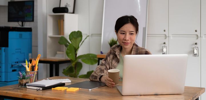 Smiling young asian teen girl video calling on laptop. Happy pretty woman student looking at computer screen watching webinar or doing video chat by webcam.