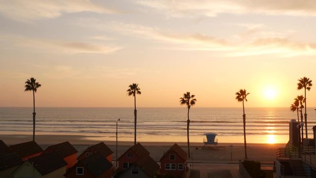 Palms silhouette sunset sky, California aesthetic. Oceanside USA. Tropical pacific ocean beach atmosphere. Los Angeles vibes. Lifeguard watchtower, palmtree and baywatch tower hut. Beachfront cottages