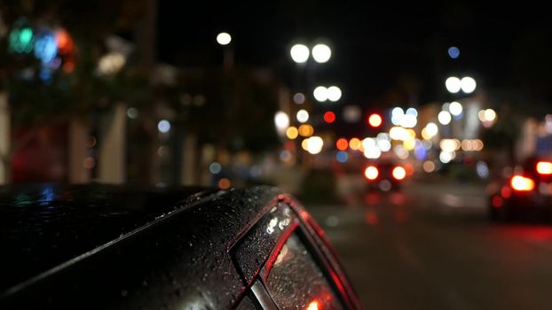 Defocused evening street, blurred bokeh. Lights of city and cars on rainy night. Reflection of electric lamps. Automobiles on road in soft focus. Twilight illuminated town, Oceanside, California USA.