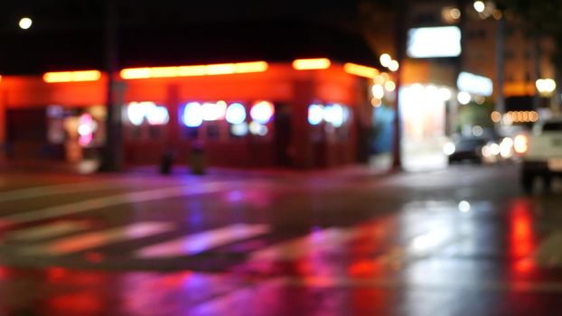 Defocused evening street, blurred bokeh. Lights of city and cars on rainy night. Reflection of electric lamps. Automobiles on road in soft focus. Twilight illuminated town, Oceanside, California USA.