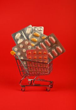 Close up several different blister packs of pills in small shopping cart over red background, concept of online medicine order delivery, low angle view