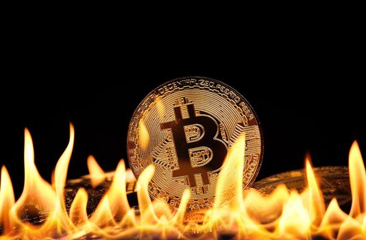Close up heap of golden bitcoin physical coins burning in fire flames over black background, as symbol of economy crisis, decline and cryptocurrency market in danger