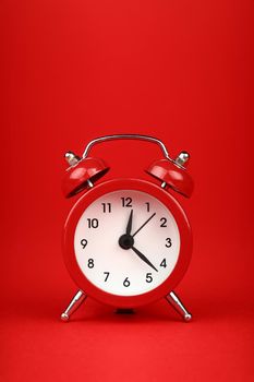 Close up one small red metal twin bell retro alarm clock over red paper background with copy space, low angle front view