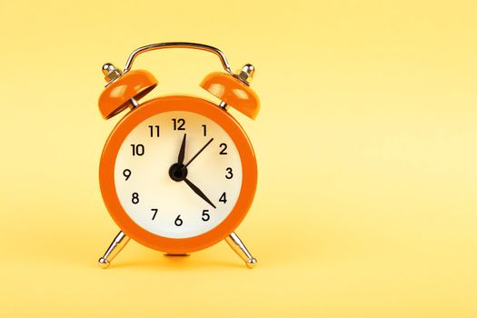 Close up one small orange metal twin bell retro alarm clock over pastel yellow paper background with copy space, low angle front view