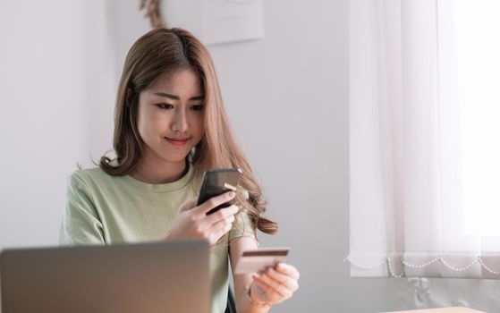 Cropped image of smiling millennial woman holding smartphone and banking credit card, involved in online mobile shopping at home, happy female shopper purchasing goods or services in internet store.