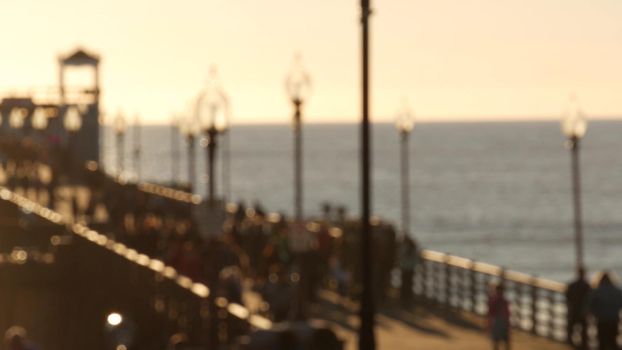 People walking, wooden pier in California USA. Oceanside waterfront vacations tourist resort. Ocean beach summertime sunset atmosphere. Blurred crowd strolling seaside boardwalk. Defocused seascape.