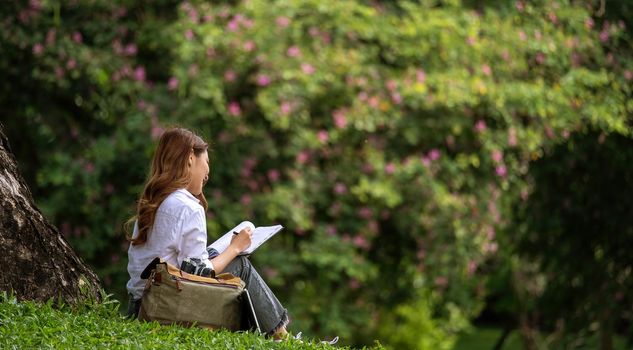 Image of joyful woman holding diary book writing note while sitting on grass in park