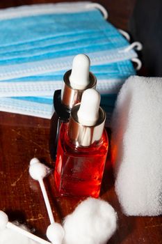 Blue and orange liquid in cosmetic droppers next to paper masks, cotton rounds and swabs with an exfoliating sponge in the background