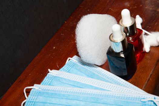 Blue and orange liquid in cosmetic droppers next to paper masks, cotton rounds and swabs with an exfoliating sponge in the background