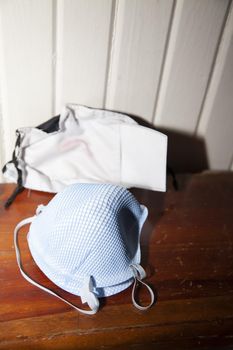 Two blue N-95 masks in front of a lipstick stained cloth mask with a filter sticking out of it