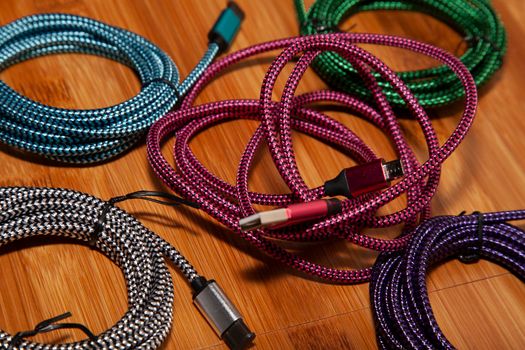 Pink charging cord in the middle of green, blue, purple, and silver charging cords on a wooden table
