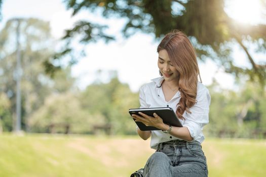 Student girl working with a digital tablet in a green park.