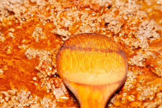 Spicy ground beef in a frying pan with a wooden spoon