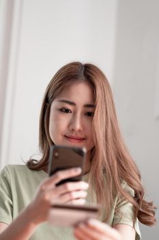 Cropped image of smiling millennial woman holding smartphone and banking credit card, involved in online mobile shopping at home, happy female shopper purchasing goods or services in internet store.