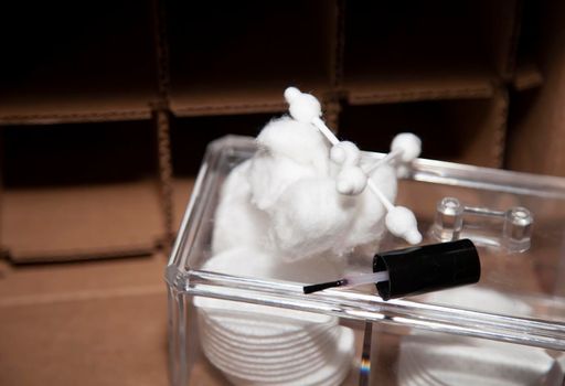 Plastic box of makeup rounds, cotton balls, and cotton swabs in front of an empty cardboard box with square storage slots