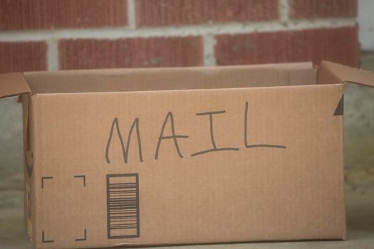 Cardboard box with the word MAIL written on it in front of a red brick house