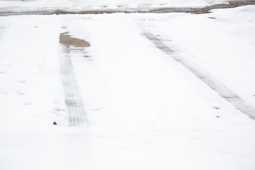 Tire tracks on a dangerously slick driveway covered in winter precipitation