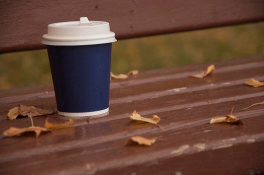 Coffee stands on a bench on the street. Cool weather. Warm up with aromatic coffee.