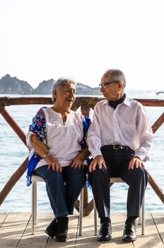 Elderly couple looking at each other laughing. Elderly couple with the sea background.