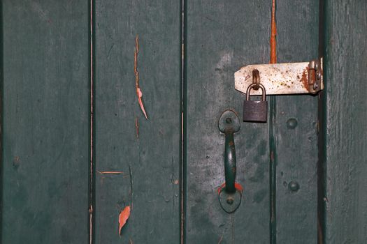 Green painted old locked wooden door with latch and padlock close-up