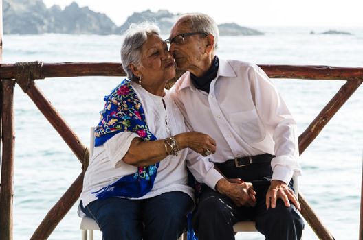 Elderly couple sitting on chairs kissing with the beach background