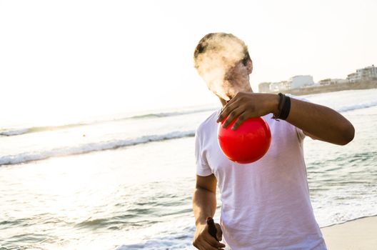 Young man with electronic cigar and a red balloon on the beach