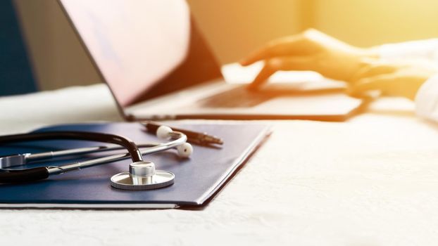 Stethoscope with file and Laptop on desk,Doctor working in hospital writing a prescription, Healthcare and medical concept