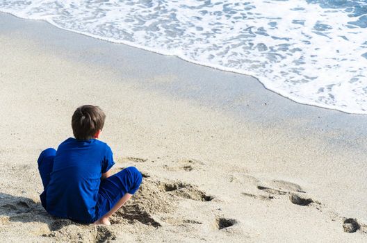 A boy looking at the sea with his back to the camera. Child looking at the sea on the beach