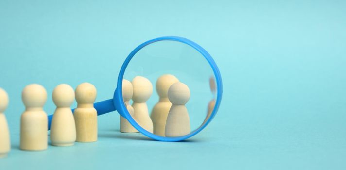 wooden figures of men stand on a blue background and a plastic magnifying glass. Recruitment concept, search for talented and capable employees, career growth, copy space