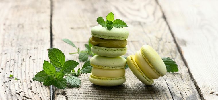 a stack of baked pistachio macarons and green mint leaves on a gray wooden table