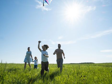 Parents and children running with kite on summer holiday vacation, perfect meadow and sky on seaside