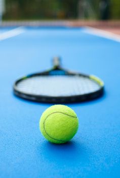 Yellow ball is laying on professional tennis racket background. A ball is on blue bright tennis cort carpet. Photo made in contrast saturated colors. Concept of sport equipment photo.