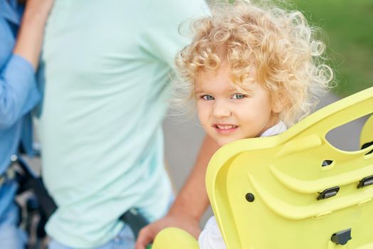 Shot of a cute little blonde haired baby girl sitting in a baby bike seat her parent hugging on the background copyspace marriage family love affection children kids parenting active lifestyle concept.