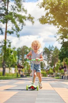 Vertical full length shot of a cute blonde little girl riding scooter at the park kids children happiness emotions activity concept.