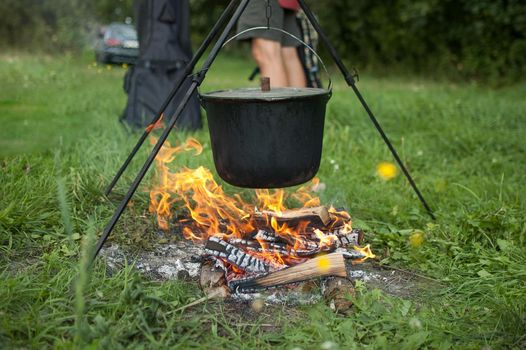 Dark big pot or cauldron, cooking pan with boiling water inside above the fire somewhere in the park or mountains, camping concept.