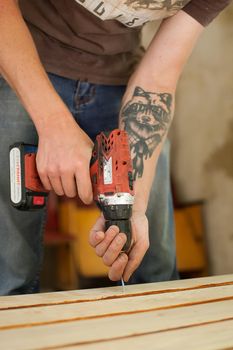 13.08.2021 - Ukraine, Goshcha, voluntary event, skilled young male worker is using power screwdriver drilling during construction wooden bench, do it yourself.