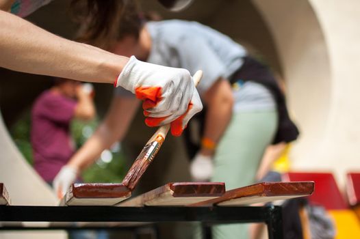 Female worker makes painting works of wooden products, plank with brown paint for making bench, carpenters work, wood covering protection