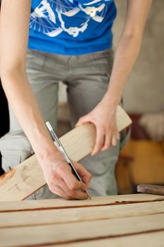 Female hands are making some marks on wooden plank for future holes using pencil for assembling bench, gender equality, feminism, do it yourself concepts