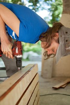 Skilled young female worker is using power screwdriver drilling during construction wooden bench gender equality, feminism, do it yourself concepts