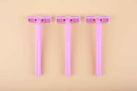 Top view of three pink razors in a row on light beige background. Concept of smooth skin, shaving and epilation