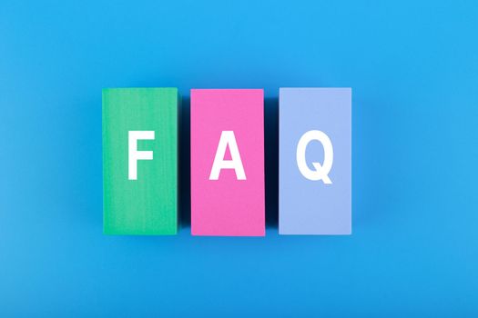 FAQ concept. Flat lay with FAQ letters on on multicolored rectangles in the middle of blue background. Creative top view of Frequently asked questions 