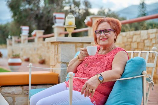 Portrait of beautiful elderly 70s woman relaxing with cup. Smiling senior female with glasses sitting in an outdoor cafe enjoying coffee. Beauty, age, health, pensioner, retired older people concept